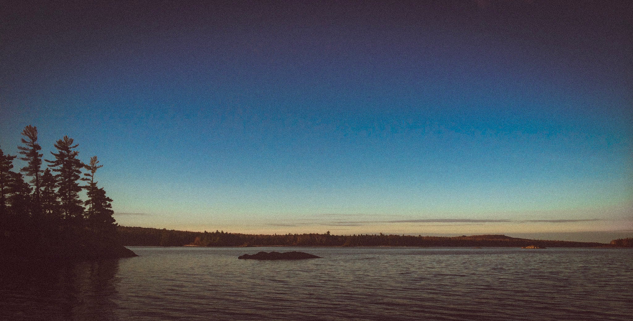 Sunrise over a placid lake with pine trees along the shoreline.